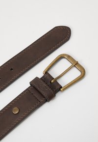 Ceinture en cuir marron avec une boucle en laiton, présentant une couture contrastante et une texture lisse. L'extrémité de la sangle se termine par une pointe arrondie.