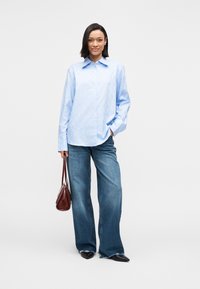 Világoskék, finom mintás hosszú ujjú ing, bő szárú farmernadrággal párosítva. Sötétbarna kézitáska. Fekete, hegyes orrú cipők.