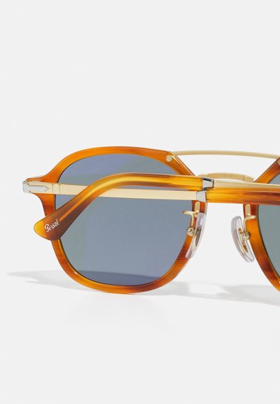 Lunettes de soleil avec une monture en acétate orange, des accents dorés et des verres gris. Présente un design à double pont et un logo gravé sur la branche.