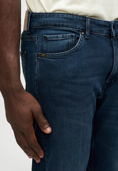 Calças de ganga azul-escuro com um corte slim. Apresentam um design tradicional de cinco bolsos, costuras discretas e um rótulo da marca na cintura.