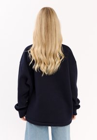 Granatowy, oversize'owy sweatshirt z opadającymi ramionami, ściągaczami u mankietów i miękką teksturą, w zestawieniu z jasnoniebieskimi spodniami o szerokich nogawkach.