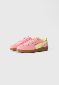 Et par rosa semskede sneakers med gule detaljer og brune gummisåler på en hvit bakgrunn.