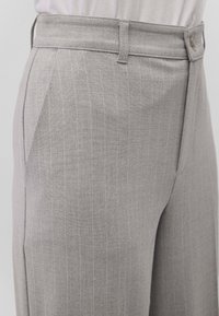 Pantaloni grigi a righe sottili con fronte piatto, tessuto testurizzato, chiusura a un bottone e passanti per cintura, che mostrano un design slim fit.
