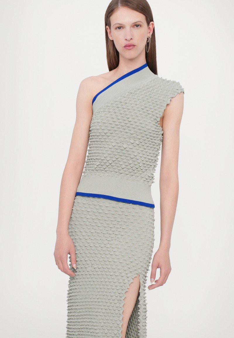 Vestido asimétrico de un solo hombro en tejido ligero gris claro con acentos de rayas azules. Presenta una abertura alta hasta el muslo y bordes en forma de concha.
