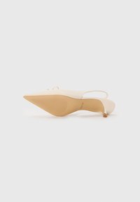 Beige slingback pump with a pointed toe, smooth upper material, thin heel, textured tan outsole, and minimalistic design details.