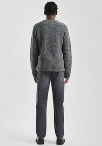 Donkergrijze gebreide trui met een textuurpatroon, gecombineerd met donkerdenimjeans. De outfit heeft lange mouwen en een losse pasvorm.