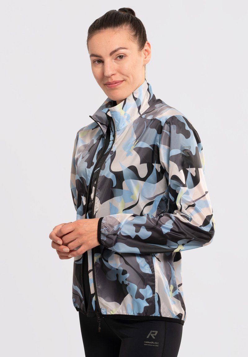 Chaqueta ligera y multicolor con un patrón de camuflaje en tonos de azul, gris y amarillo. Tiene un cuello alto y cierre de cremallera.