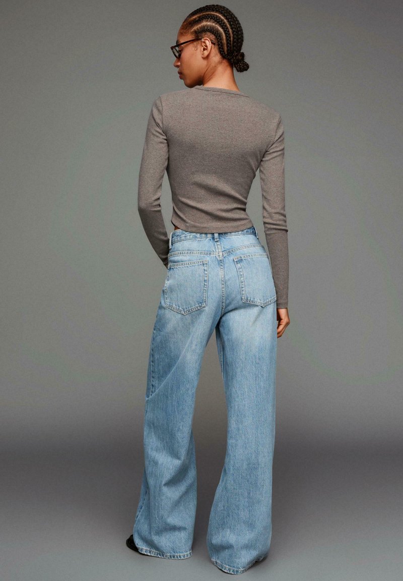 Sivý dlhý rukáv s rebrovaným dizajnom v kombinácii so svetlomodrými nohavicami s vysokým pásom a širokými nohavicami. Denim má klasickú pranie s zadnými vreckami a minimálnymi švovými detailmi.