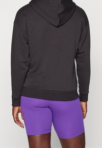 Felpa nera in cotone con tasca frontale e cappuccio, abbinata a pantaloni sportivi viola con una vestibilità aderente.