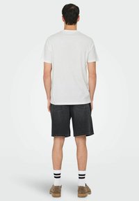 White cotton t-shirt, black denim shorts, knee-length. White socks with black stripes, brown shoes. Simple, casual outfit.