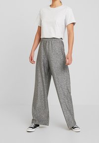 Grijze t-shirt met korte mouwen en wijde zilveren glitterbroek met elastische tailleband en zijzakken, gecombineerd met zwarte sneakers.