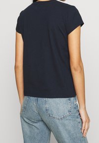 Camiseta de algodón azul marino con mangas cortas, cuello redondo y corte relajado, combinada con jeans de tiro alto de color azul claro.