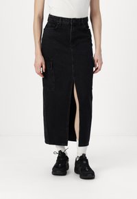 Svart denim midi-skjørt med frontsplitt, flere lommer, høy midje og rett snitt, komplettert med svarte sneakers og hvite sokker.