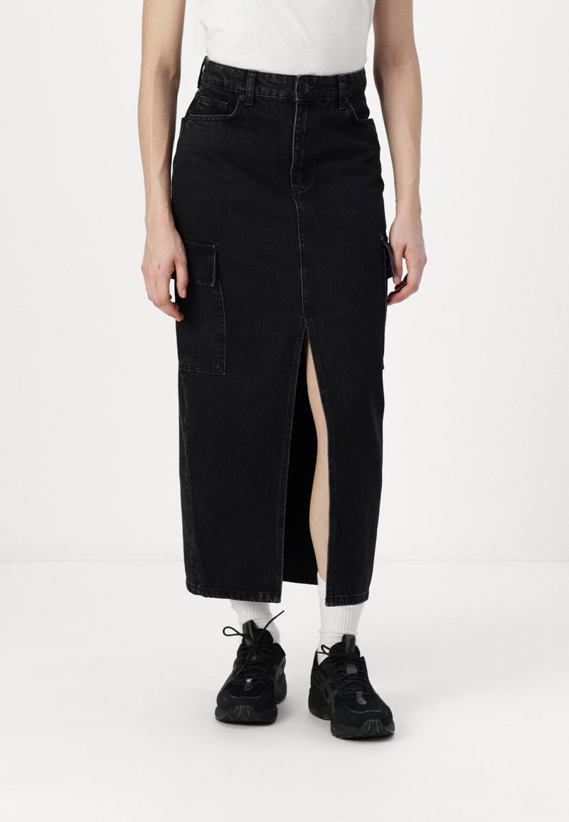 Svart denim midi-skjørt med frontsplitt, flere lommer, høy midje og rett snitt, komplettert med svarte sneakers og hvite sokker.
