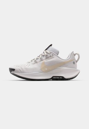 Nike løbesko i hvid, med en struktureret mesh-overdel, en beige swoosh-logo, en sort sål og en trækflap ved hælen for nem påtagning.