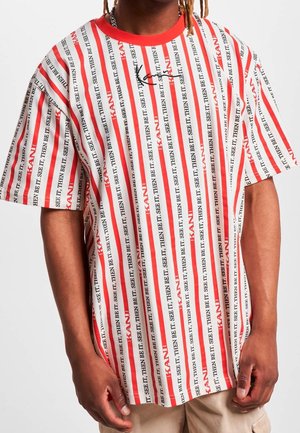 Hvid oversized t-shirt med lodrette striber i rød og sort tekst, rød krave og korte ærmer med sorte detaljer.