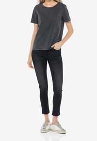 T-shirt grigia a maniche corte con collo rotondo, abbinata a jeans skinny scuri e scarpe da ginnastica bianche, evidenziando un look casual.