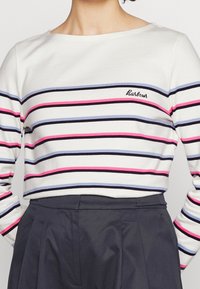 Gestreifte Langarmbluse in Weiß, mit horizontalen Streifen in Marineblau, Pink und Blau, sowie einem gestickten Logo auf der Brust.