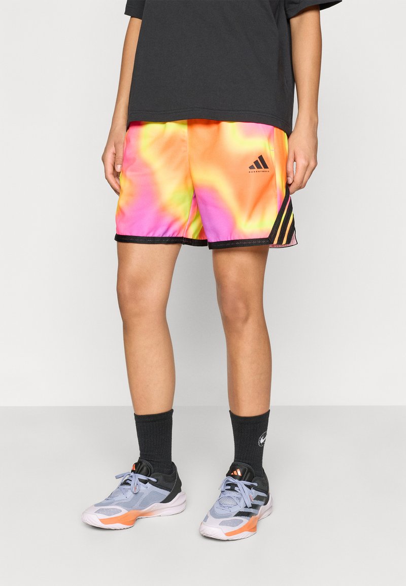 Farverige tie-dye basketballshorts i nuancer af pink, orange og gul med sorte detaljer og Adidas-logo; kombineret med grå sko og sorte sokker.