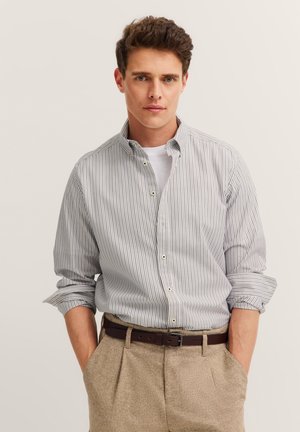 Striped button-up shirt in light blue and white, with a collar and rolled-up sleeves. Paired with beige trousers and a brown belt.