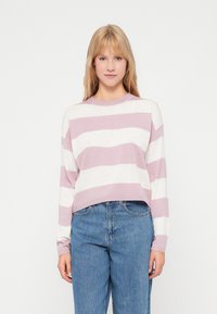 Un pull court rayé rose clair et blanc en maille douce avec des manches longues et un col rond, associé à un jean bleu taille haute.