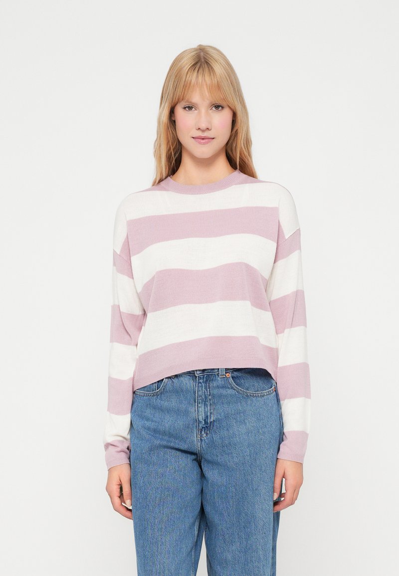 Un pull court rayé rose clair et blanc en maille douce avec des manches longues et un col rond, associé à un jean bleu taille haute.