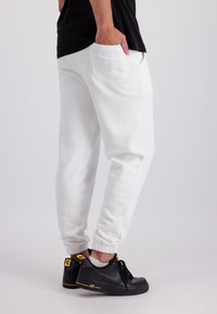 Witte katoenen joggers met elastische boorden en zijzakken, gecombineerd met zwarte sneakers met gele accenten en een grijs logo.