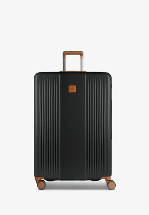 Valise noire rigide avec texture striée verticale, poignée et accents marron, quatre roues pour la mobilité, fermeture éclair et détails de logo.