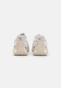 Baskets de sport avec une tige en cuir blanc, des accents en suede beige et une semelle extérieure en caoutchouc texturée. Présente un logo doré et un col rembourré.