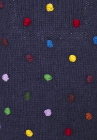 Tissu tricoté bleu marine avec des points en relief multicolores en rouge, jaune, bleu, vert, violet et marron, créant un motif texturé.