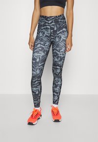 Legginsy w czarno-szary wzór, wykonane z elastycznego materiału, z wysokim stanem, połączone z jasnopomarańczowymi butami sportowymi.