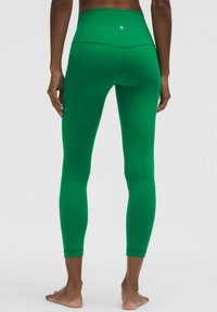 Zaļas augstās leggingas, kas izgatavotas no elastīga auduma, ar gludu tekstūru un pieguļošu dizainu, aizmugurē ar mazu logotipu.