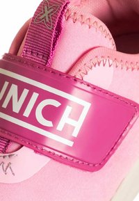 Scarpa sportiva rosa con una parte superiore in tessuto testurizzato, una fascia di plastica lucida e un logo bianco prominente. Fodera morbida e dettagli cuciti.