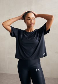 Svart trenings-T-skjorte med korte ermer, laget av et glatt stoff; kombinert med svarte leggings med hvite logo-detaler.