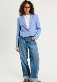 Veste en lin bleue raccourcie à un bouton, associée à un jean en denim bleu clair taille haute avec une coupe large et des ourlets roulés.