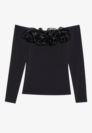 Top negro sin mangas con largas mangas, que presenta un borde floral texturizado de terciopelo negro a lo largo del escote.