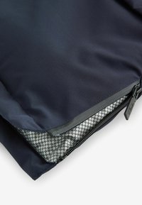 Tissu bleu foncé avec une fermeture éclair partiellement ouverte révélant une doublure intérieure grise à motif de grille composée de petits cercles noirs.