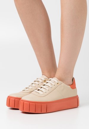 Beżowe skórzane sneakersy z teksturowaną pomarańczową podeszwą na platformie. Cechy to białe sznurowadła i okrągłe złote oczka.