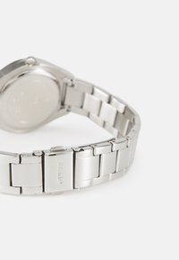 Silver stainless steel watch with a smooth round case and a link bracelet. Features a clasp with the logo "GUESS" engraved.
