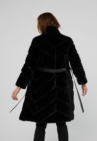 Cappotto in pelliccia sintetica nera con motivo a zigzag, maniche lunghe e cintura coordinata, colletto alto e texture morbida.