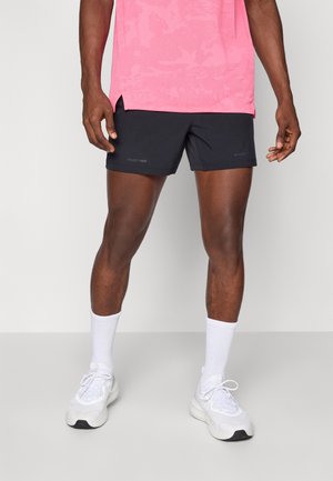 Shorts de atletism negri cu o textură netedă, asortați cu o cămașă roz cu model și șosete albe. Pantofii sunt albi cu o formă rotunjită.