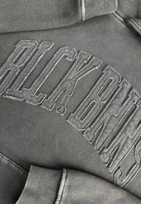 Grijze sweatshirt met verhoogde borduring waarop "BLCK BNS" staat. Heeft ribgebreide cuffs en een zachte, gestructureerde stof met een casual fit.