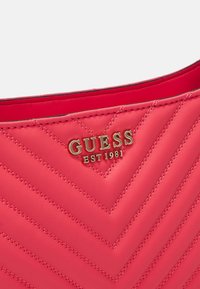 Lyserød quiltet håndtaske lavet af syntetisk læder, med et chevron-mønster og et gyldent "GUESS EST 1981" logo akcent.
