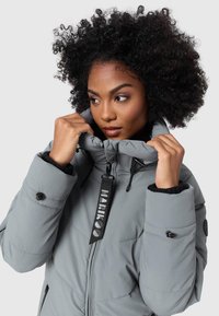 Veste en duvet grise avec un col montant, dotée de poches zippées, d'une sangle avec logo noir et d'une texture matelassée. Agrémentée de boutons durables.