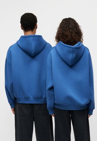 Μπλε φούτερ με κουκούλα και άνετη εφαρμογή, με ριμπ μανσέτες και τελειώματα, σε συνδυασμό με μαύρο φαρδύ τζιν.