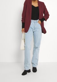 Blazer bordeaux sopra una maglietta nera a coste, jeans dritti blu chiaro e stivaletti neri con tacco block. Inclusa borsa bianca.