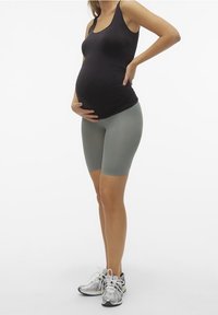 Zwarte mouwloze tanktop, lichtgroene shorts en grijze sneakers. De figuur is gepositioneerd met een ronde buik, wat het strakke ontwerp benadrukt.