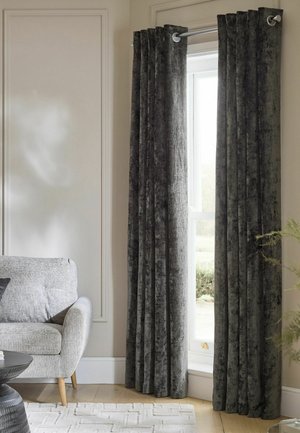 Dark gray velvet curtains hanging on a metal rod beside a tall window with light coming through, next to a gray fabric armchair.