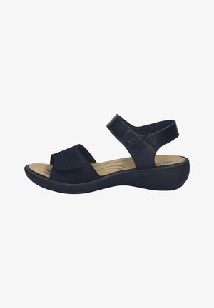 Sort sandal med åben tå, justerbare remme, polstret beige indersål og lav kilehæl for komfort og støtte.