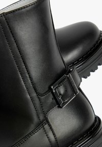 Zwarte leren enkellaarzen met een gladde textuur, een zijgesp accent en een robuuste profielzool voor verbeterde grip en stabiliteit.